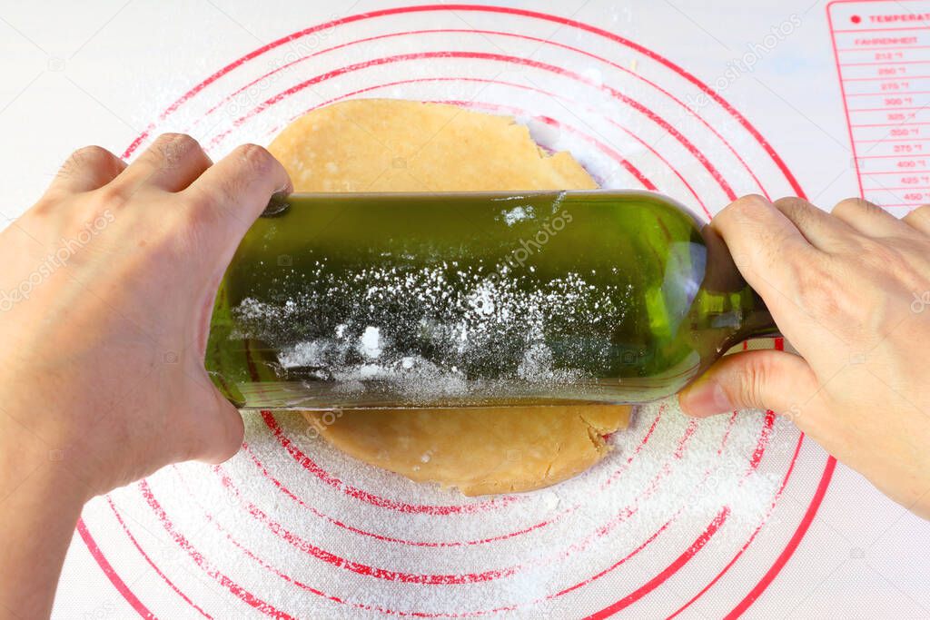 Hand rolling pie dough with an empty wine bottle for the concept of amateur cook baking at home