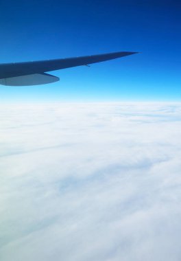 Canlı mavi gökyüzünde, uçak penceresinden görülebilen bulutlarla dolu bir kanat.