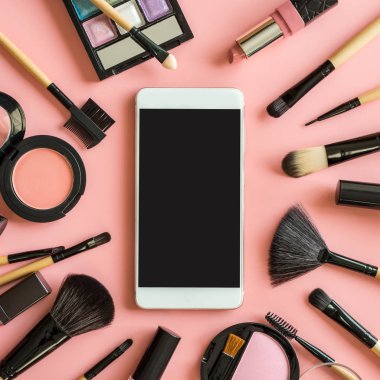 Fırçalar ve akıllı telefon ve kopya alanı ile pembe arka plan üzerinde kozmetik makyaj seti