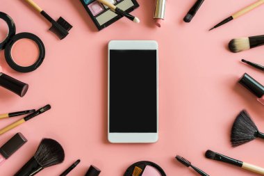 Fırçalar ve akıllı telefon ve kopya alanı ile pembe arka plan üzerinde kozmetik makyaj seti
