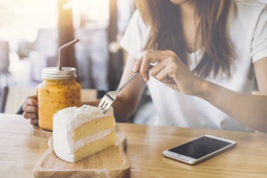 Akıllı telefon kullanarak ve cafede pasta yemeye genç kadın
