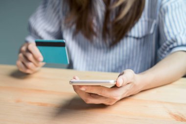 Bir kredi kartı tutan ve online alışveriş için smartphone kullanarak genç kadın