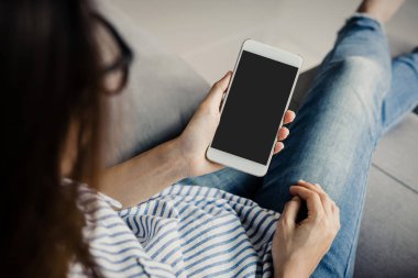 Genç kadın gözlük siiting kanepe ve akıllı telefon evde kullanma