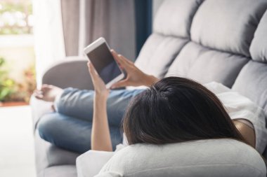 Oturma odasında kanepede rahat evde Smartphone kullanarak genç kadın