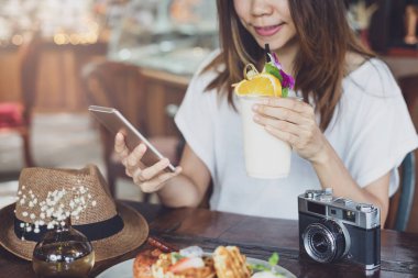 Young woman using smart phone and enjoy eating dessert in cafe o