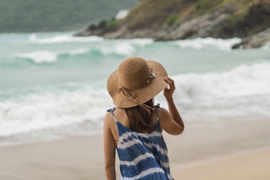 Rüzgarlı bir günde sahilde tek başına duran genç bir gezgin kadın.