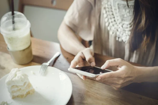 Fiatal nő használ szúró telefon, és enni tortát, kávézó — Stock Fotó
