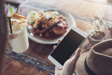 Akıllı telefon kullanan genç kadın ve kafede tatlı yeme keyfini çıkarın