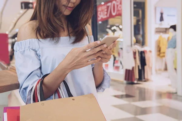 Jonge vrouw met boodschappentassen met behulp van Smart Phone en winkelen in — Stockfoto