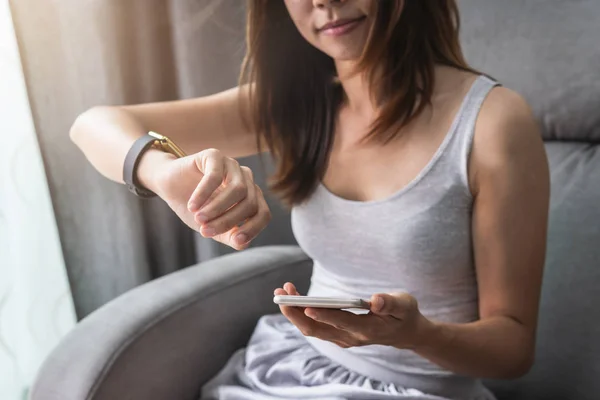 Молода азіатська жінка використовує смарт-годинник і смартфон вдома — стокове фото
