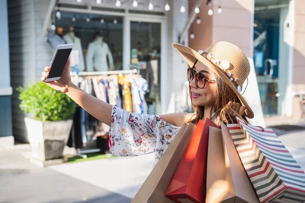 Jonge vrouw met boodschappentassen met smartphone voor selfie bij sh — Stockfoto