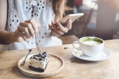 Akıllı telefon kullanan ve pasta yiyen genç kadın