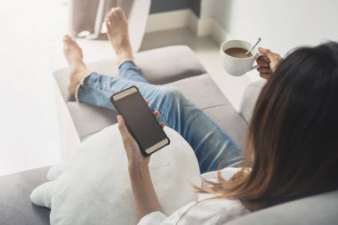 Oturma odasında kanepede rahat evde Smartphone kullanarak genç kadın