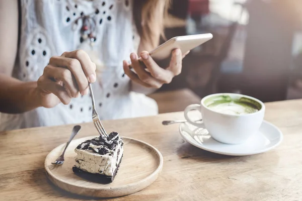 Young woman using smart phone and eating cake