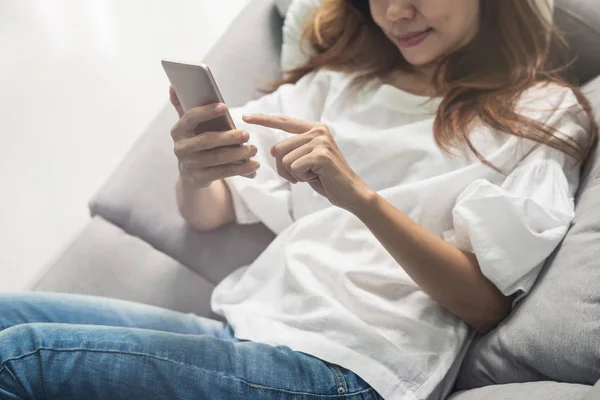 Молода жінка використовує смартфон в затишному будинку на дивані у вітальні — стокове фото