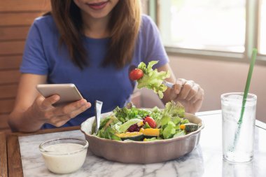 Akıllı telefon kullanan ve restoranda yemek yiyen genç kadın