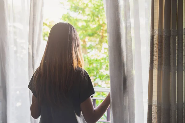 Junge asiatische Frau enthüllt Vorhang und schaut aus dem Fenster in th — Stockfoto