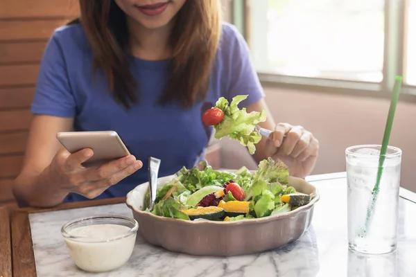 Akıllı telefon kullanan ve restoranda yemek yiyen genç kadın