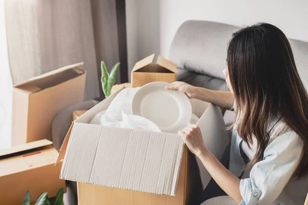 Mujer feliz joven moviéndose en un nuevo hogar y desempacando la caja de cartón — Foto de Stock
