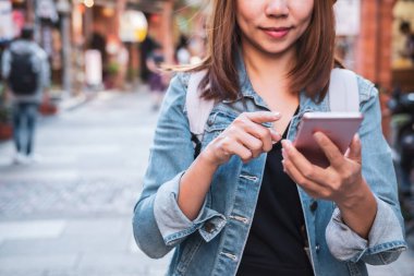 Genç bayan gezgin alışveriş caddesinde yürüyor ve akıllı telefonu konum aramak için kullanıyor, seyahat yaşam tarzı konsepti