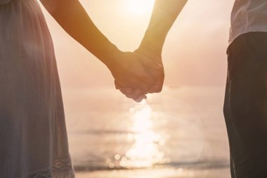 Genç kadın gezgin erkeğin elini tutuyor ve kumsalda gün batımını seyrediyor yaz tatilinde olan bir çift.