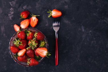 Kırmızı çatallı bir çilek ve siyah kırsal arka plandaki kristal kasede. Üst Manzara. Dikey. Diyet asgari konsepti.