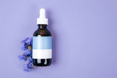 Esaslı bir yağ şişesi. Arka planda taze mor çiçekler var.