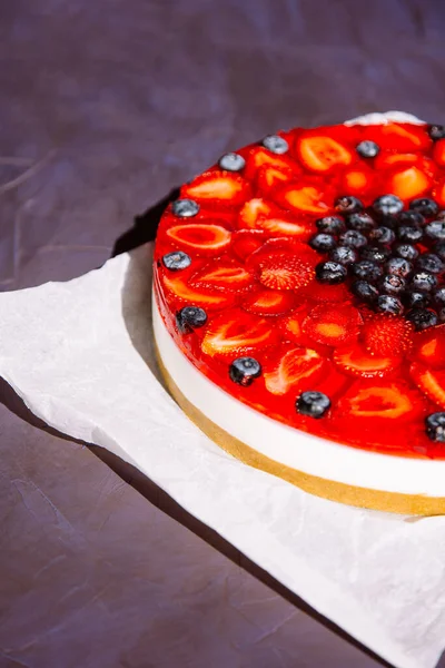 Cold cheesecake with strawberry and blueberry and strawberry jelly on top.