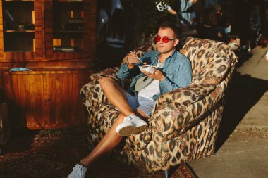 Eski sandalyede oturan bir adam müzik festivalinde yemek yiyor. Sokak yemeği yiyen mutlu adam.