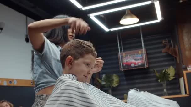 Zabawny chłopak odwiedził zakład fryzjerski. Piękna ormiańska fryzjerka robi fryzurę. 4K — Wideo stockowe
