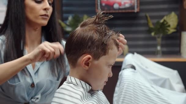 En rolig pojke besökte frisersalongen. Vacker armenisk kvinna frisör gör en frisyr. 4K — Stockvideo