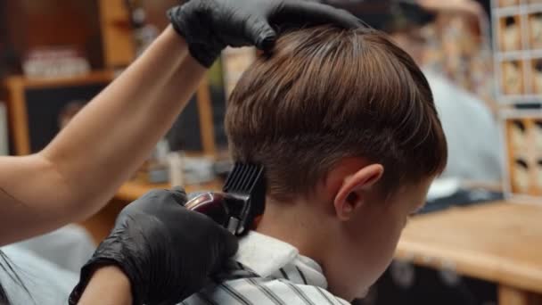 Seorang anak laki-laki yang lucu mengunjungi salon. Penata rambut wanita Armenia yang cantik membuat potongan rambut. 4K — Stok Video