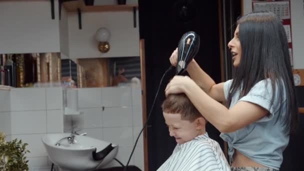 Un chico gracioso visitó la peluquería. Hermosa peluquera armenia hace un corte de pelo. 4K — Vídeos de Stock