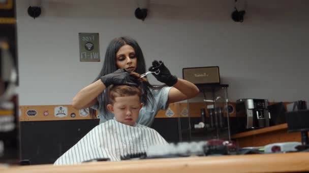 Een grappige jongen bezocht de kapperszaak. Mooie Armeense vrouw kapper maakt een kapsel. 4K — Stockvideo
