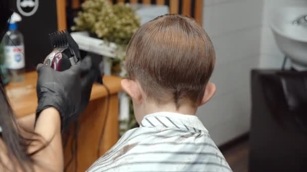 Un drôle de garçon a visité le salon de coiffure. Belle coiffeuse arménienne fait une coupe de cheveux. 4K — Video