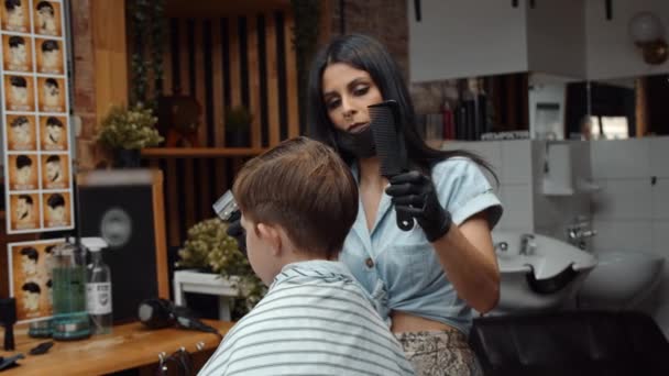 Un chico gracioso visitó la peluquería. Hermosa peluquera armenia hace un corte de pelo. 4K — Vídeos de Stock