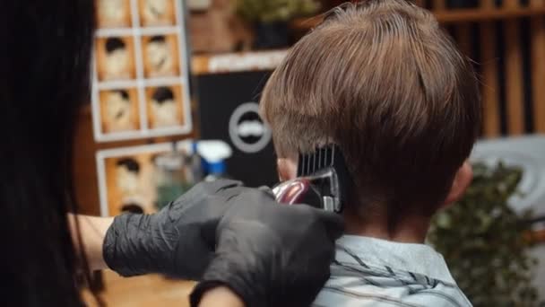 Un ragazzo divertente ha visitato il barbiere. Bella parrucchiera donna armena fa un taglio di capelli. 4K — Video Stock