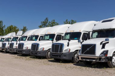 Indianapolis - Circa June 2020: Freightliner and Volvo Semi Tractor Trailer Trucks Lined up for Sale. Freightliner is owned by Daimler. clipart
