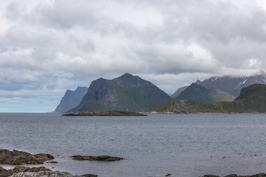 Norveç fiyortlarının bulutlu gökyüzü ve seçici odak noktalarıyla çevrili turkuaz su manzarası