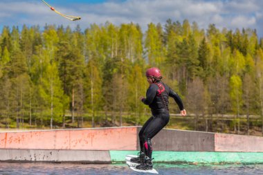 Fagersta, İsveç - Maj 26, 2020: Wakeboardlu genç kız Wakeboard 'da aşırı atlama yapıyor, etrafta bir sürü sıçrama oluyor. Bir genç kask kullanır. Wakeboard ekstrem bir spordur..