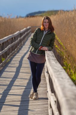 Kızıl saçlı kız, tahta bir geçitin korkuluklarına yaslandı. Kameraya bak..