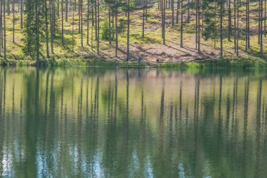 Bulutlu gökyüzü ve gölün kenarındaki tenha alanda ağaç yansıması. Sakin sular ve bulutlu gökyüzü. İsveç 'in arka planında bir balıkçı. Seçici odaklanma. uzun pozlama