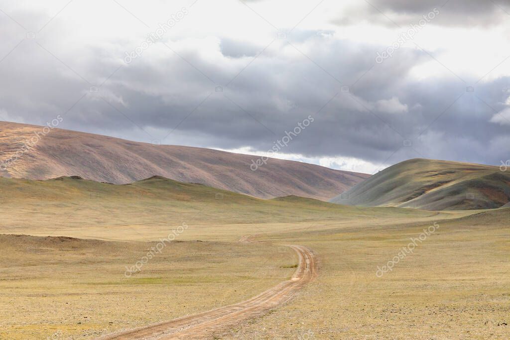 Winding dirt road through lush rolling hills of Central Mongolian steppe. Mongolian Altai. Typical view of Mongolian landscape.