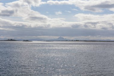 Norveç fiyortlarının bulutlu gökyüzü ve seçici odak noktalarıyla çevrili turkuaz su manzarası