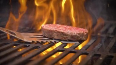 Hamburger pirzolası barbekü ızgarasında ters dönmüş. Yanan kömürden çıkan ateş.