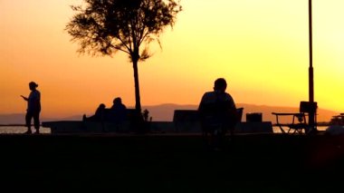İnsanlar gün batımında yürür, bisiklete biner ve dinlenme alanında bir sandalyeye otururlar.
