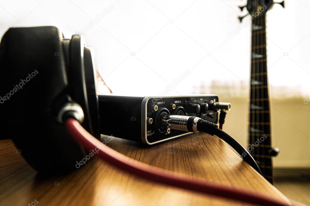 Headphone and soundacard on the table and a bass guitar on the background.