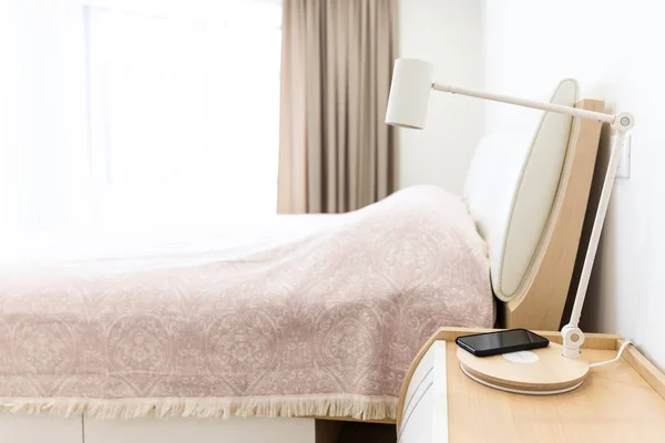 Ricarica smartphone wireless su lampada vicino al letto — Foto Stock