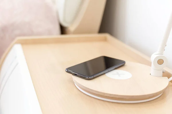 Wireless smartphone charging on lamp near bed — Stock Photo, Image