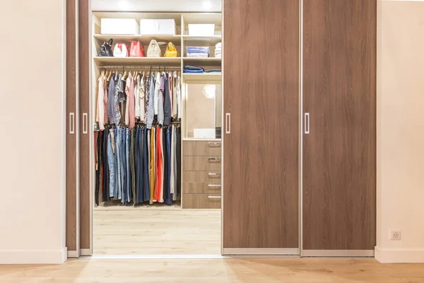 Modern wooden wardrobe with clothes hanging on rail in walk in closet — Stock Photo, Image